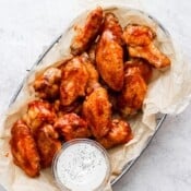 A metal basket full of bbq chicken wings and a small dish of ranch dressing.