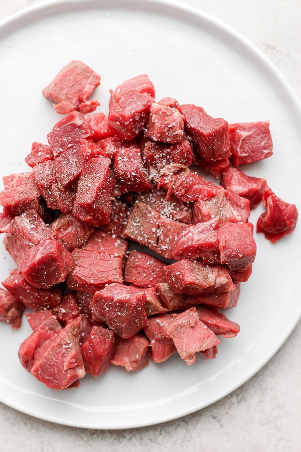 Chunks of round steak on a white plate with salt and pepper sprinkled on top.