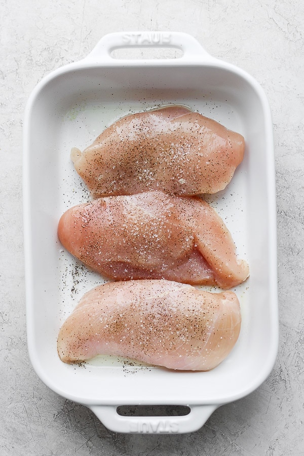 Raw, seasoned chicken breasts in a baking dish.