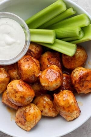A bowl of buffalo chicken meatballs with celery sticks and a bowl of ranch dressing.