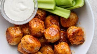 A bowl of buffalo chicken meatballs with celery sticks and a bowl of ranch dressing.