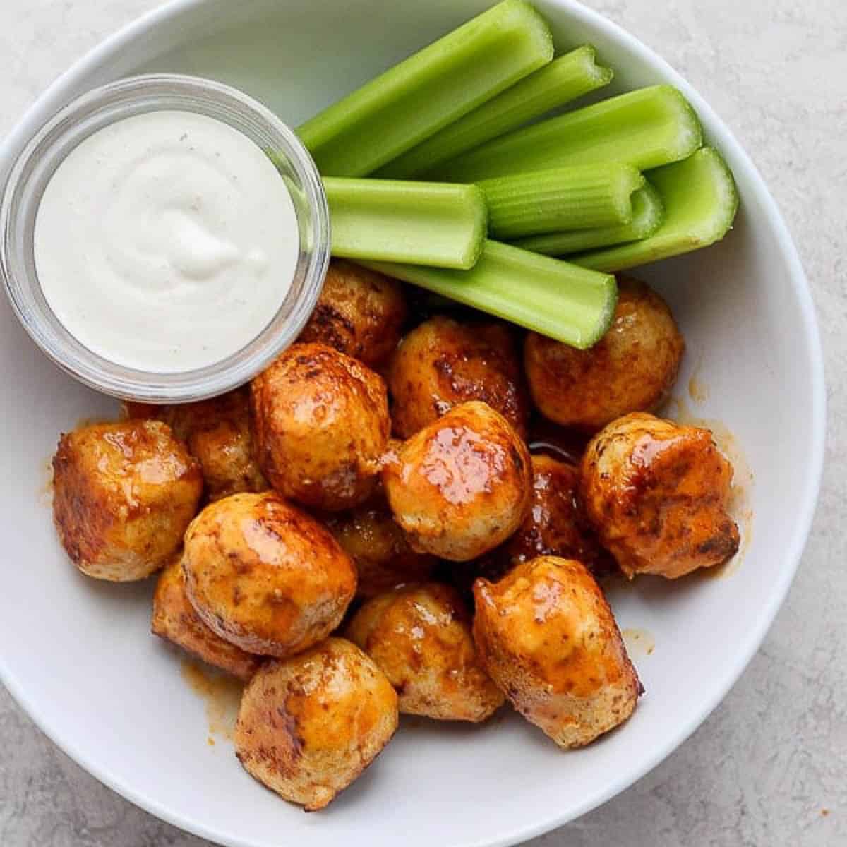 A bowl of buffalo chicken meatballs with celery sticks and a bowl of ranch dressing.
