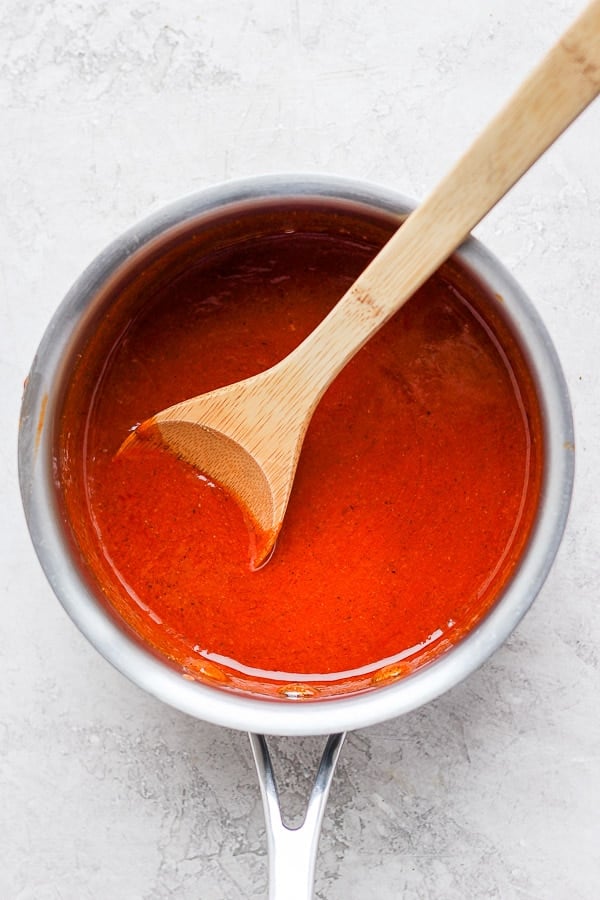 Buffalo sauce in a small saucepan with a wooden spoon.