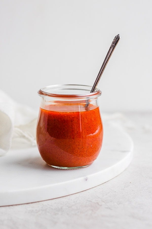 Buffalo sauce in a small glass jar with a spoon in it.