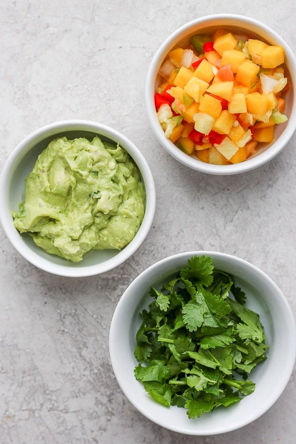 Mango salsa, guacamole, and cilantro in separate bowls.