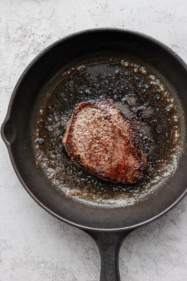 A steak being seared in a cast iron skillet.