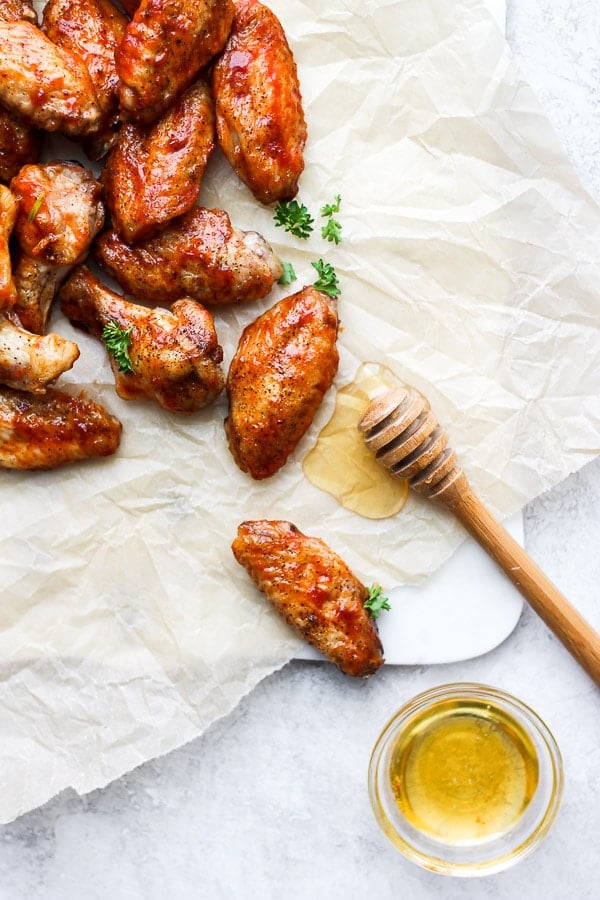 Honey bbq wings on a piece of parchment paper next to a honey stick.