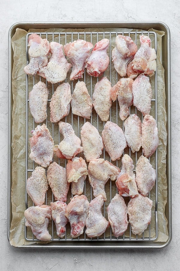 Raw chicken wings on a prepared wire rack and baking sheet with salt and pepper on them.