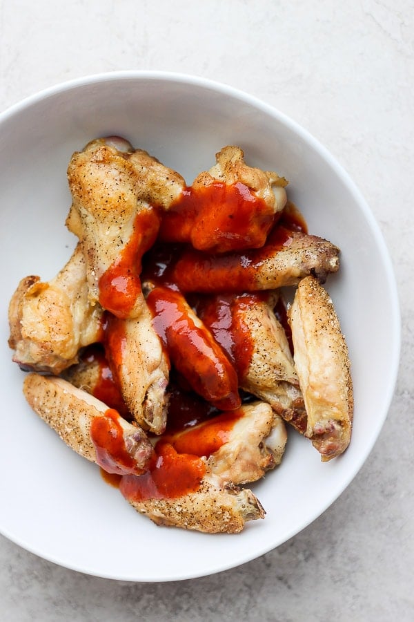 Cooked chicken wings in a white bowl with the bbq and honey sauce on top.