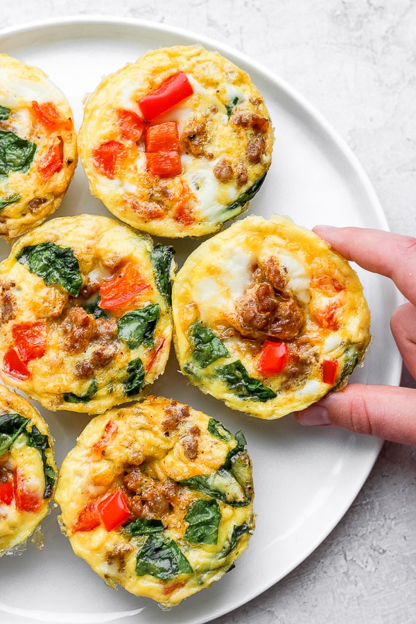 Baked egg cups on a plate with someone grabbing one. 