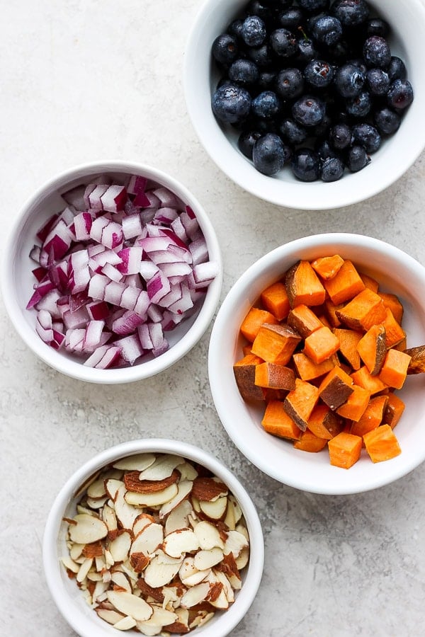 Four bowls filled with blueberries, red onion, sweet potato and slivered almonds. 