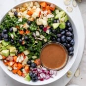 A massaged kale salad in a white bowl with a small dish of balsamic dressing.