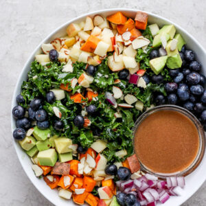 A large bowl of massaged kale salad with a small dish of dressing.