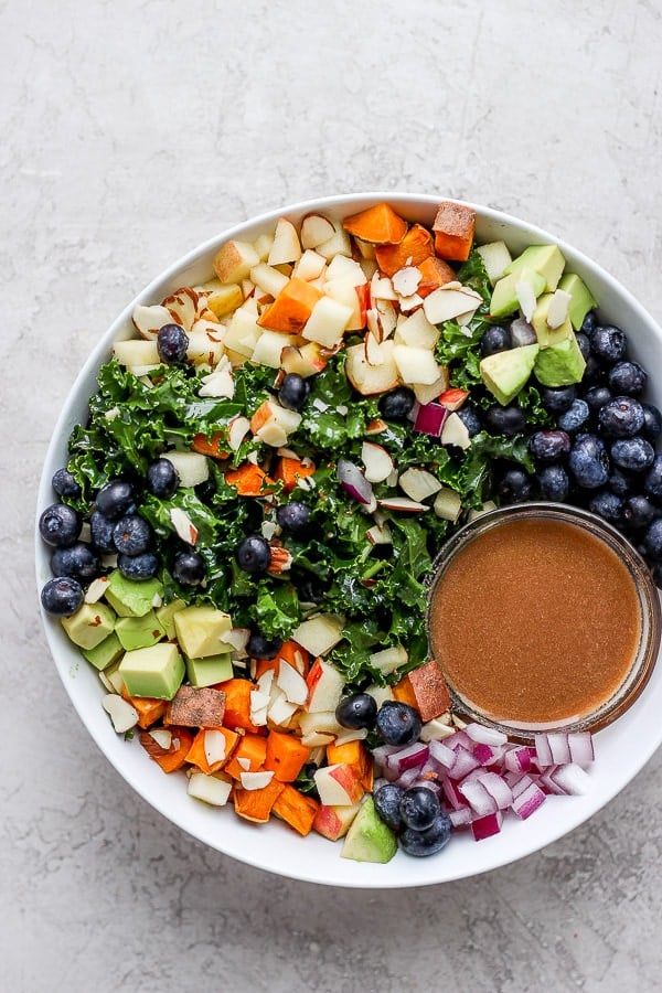mBowl of massage kale salad that is filled with sweet potatoes, blueberries, avocado, apple and slivered almonds. 