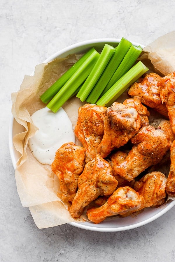 Buffalo chicken wings with some ranch dressing and celery sticks.