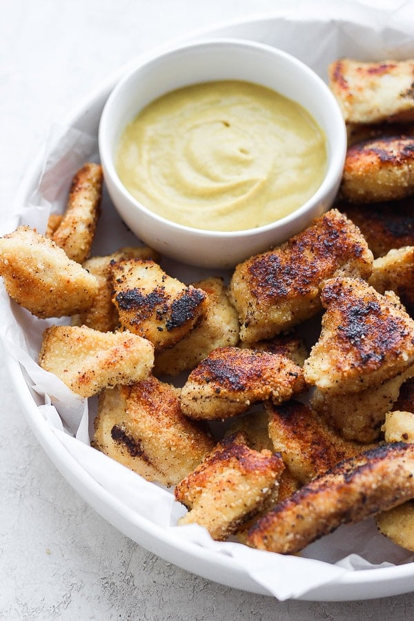 A batch of chicken nuggets with some mustard dip.
