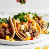 A plate of pulled pork tacos with someone squeezing a lime on top.