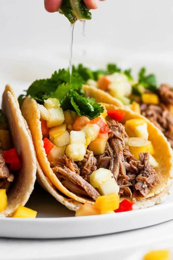 A plate of pulled pork tacos with someone squeezing a lime on top.