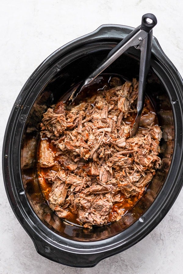 A slow cooker with pulled pork inside. 