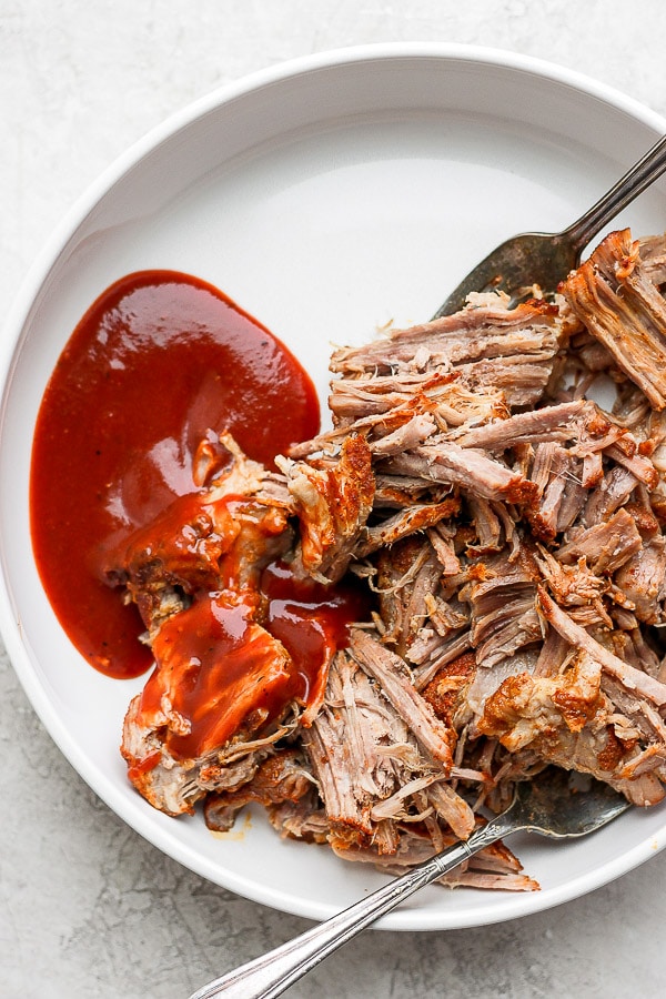 Pulled pork on a white plate with BBQ sauce and a fork.