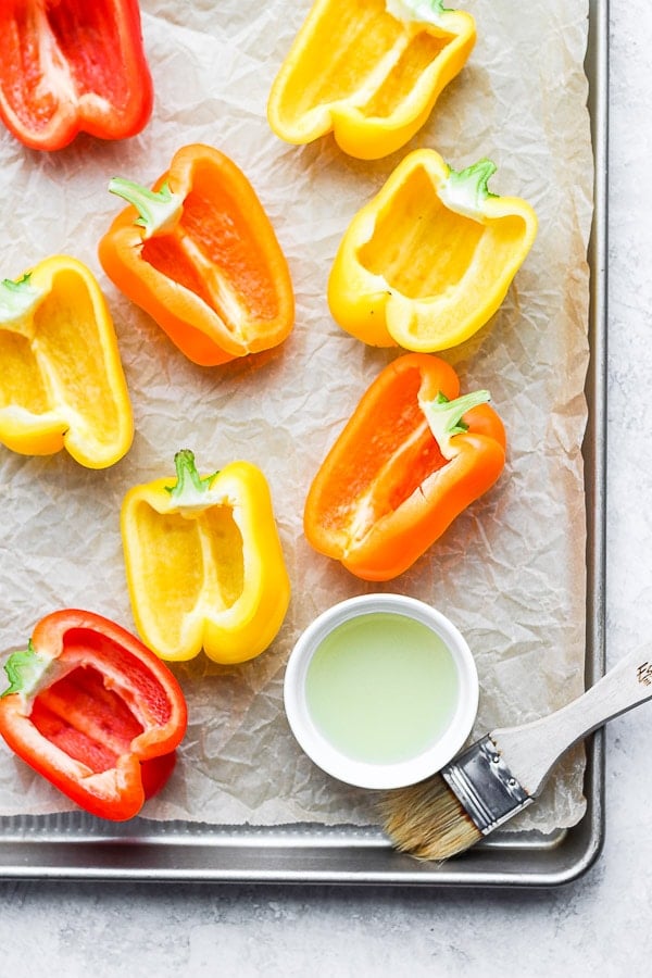 Bell peppers prepped for stuffing on a cookie sheet.