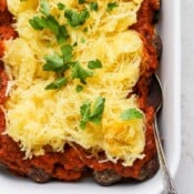 A white baking dish of baked spaghetti squash and meatballs with a spoon sticking out the side.