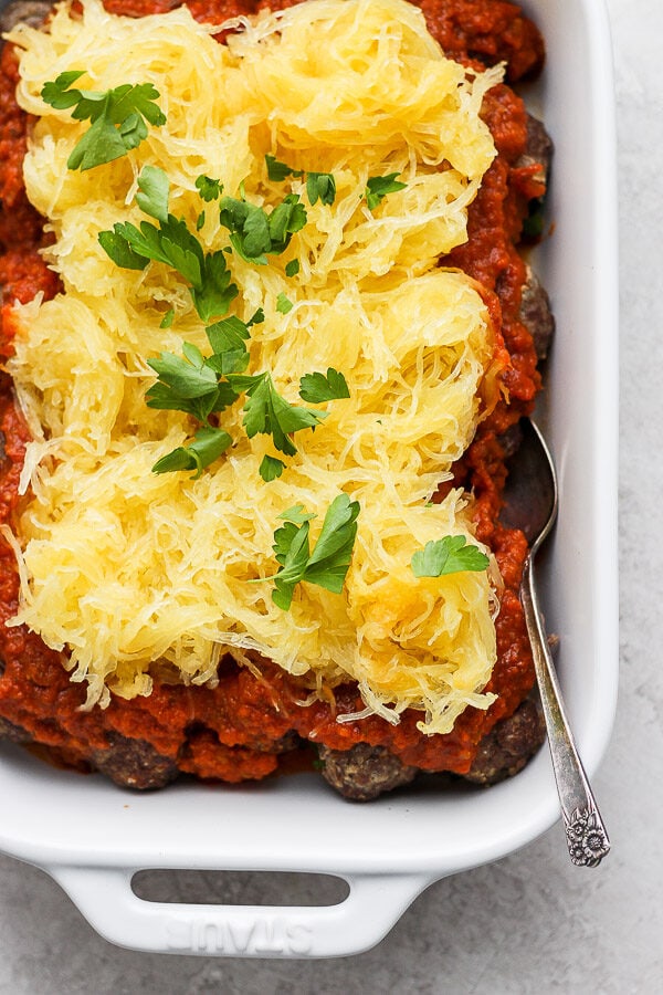 A white baking dish of baked spaghetti squash and meatballs with a spoon sticking out the side.