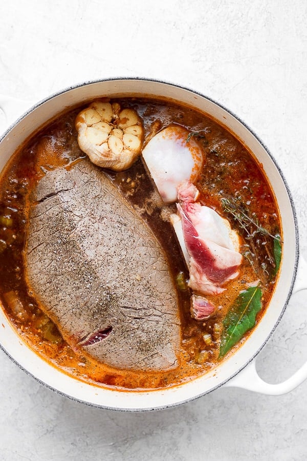 The beef broth mixture, garlic, beef bones, beef broth, pomegranate juice, tapioca starch, bay leaves, vinegars, and thyme added to the pot along with returning the roast too.