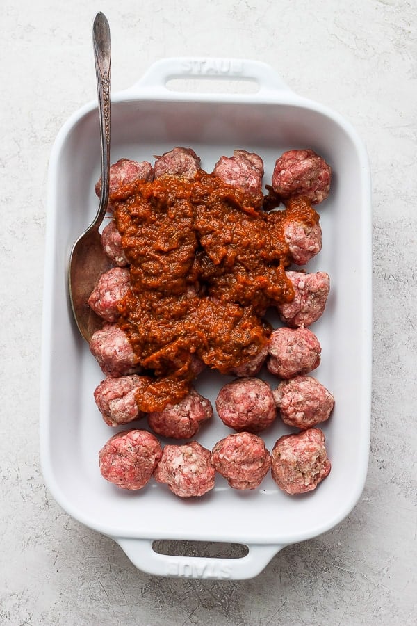 Meatballs and sauce in a baking dish before baking.