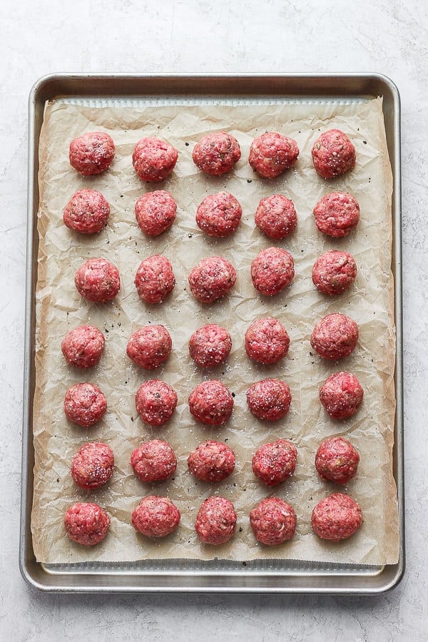 Meatballs on a parchment-lined baking pan before cooking.