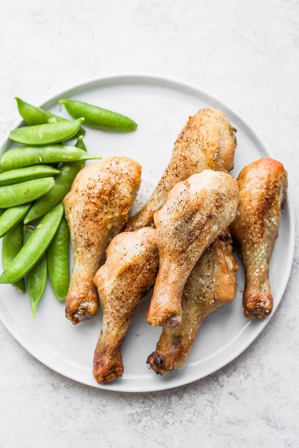 Drumsticks on a white plate with sugar snap peas.