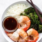 A bowl of sheet pan shrimp and broccoli in a bowl of cauliflower rice with soy sauce.