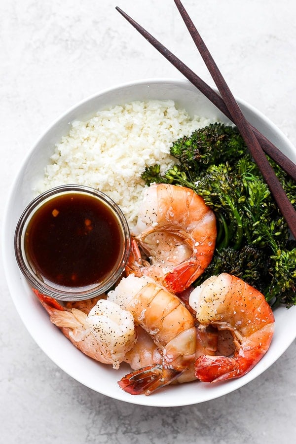 A bowl with cauliflower rice, shrimp, broccoli and a little bowl of paleo teriyaki sauce.