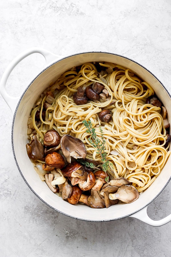 Cooked fettuccini noodles placed into the large pot with stroganoff sauce and mushrooms.
