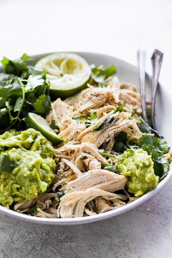 A white bowl full of shredded cilantro lime chicken with fresh toppings.