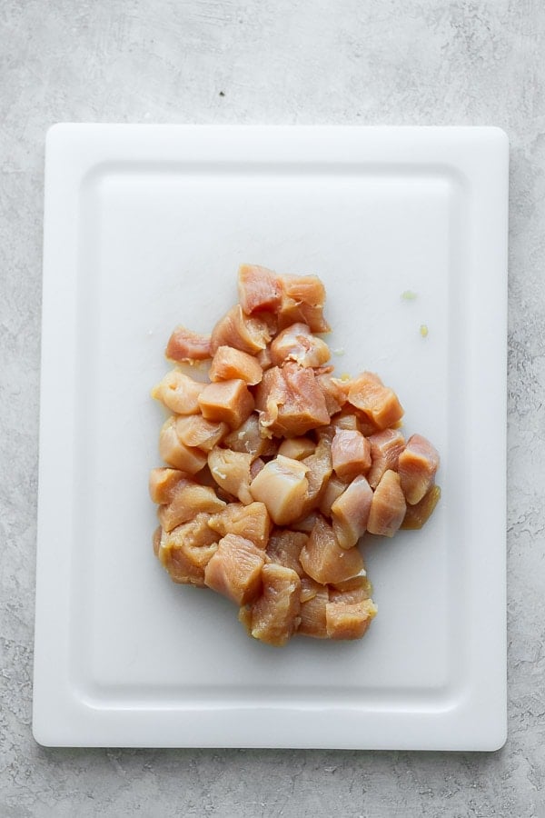 Chicken breasts cut up into pieces on a white cutting board.