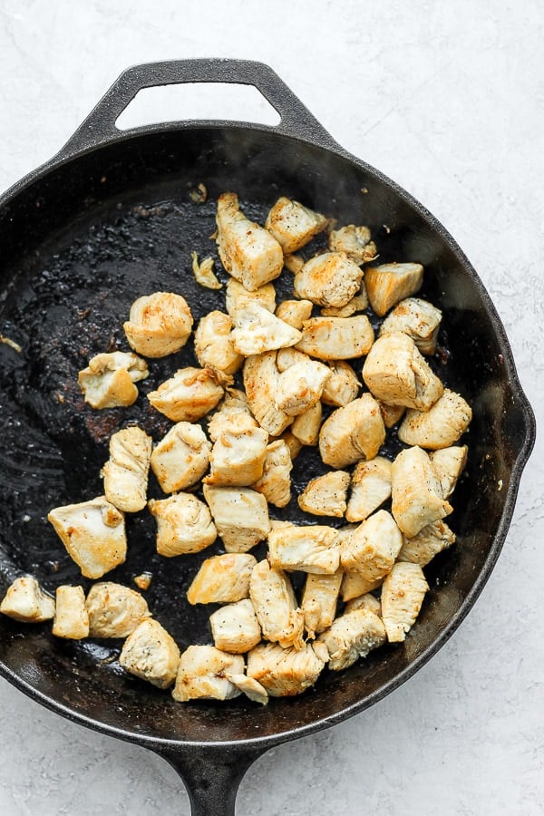 Chicken pieces cooking in a cast iron skillet. 