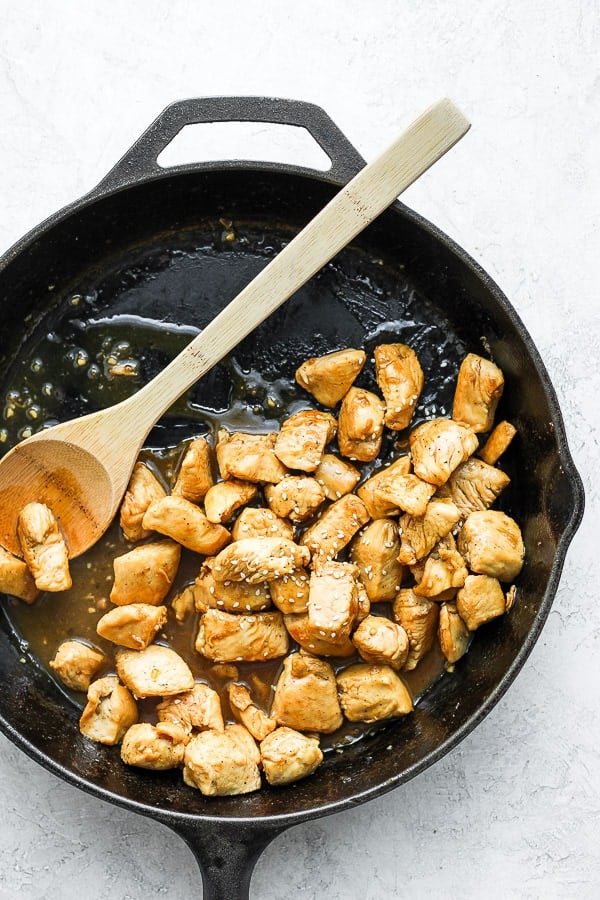 Chicken cooking in a cast iron skillet with orange sauce.