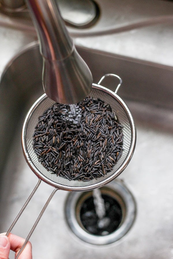 Wild rice being rinsed under cold running water.