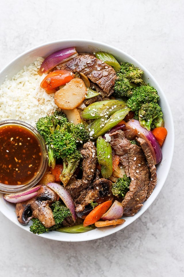 Steak stir fry on a bed of rice in a white bowl.