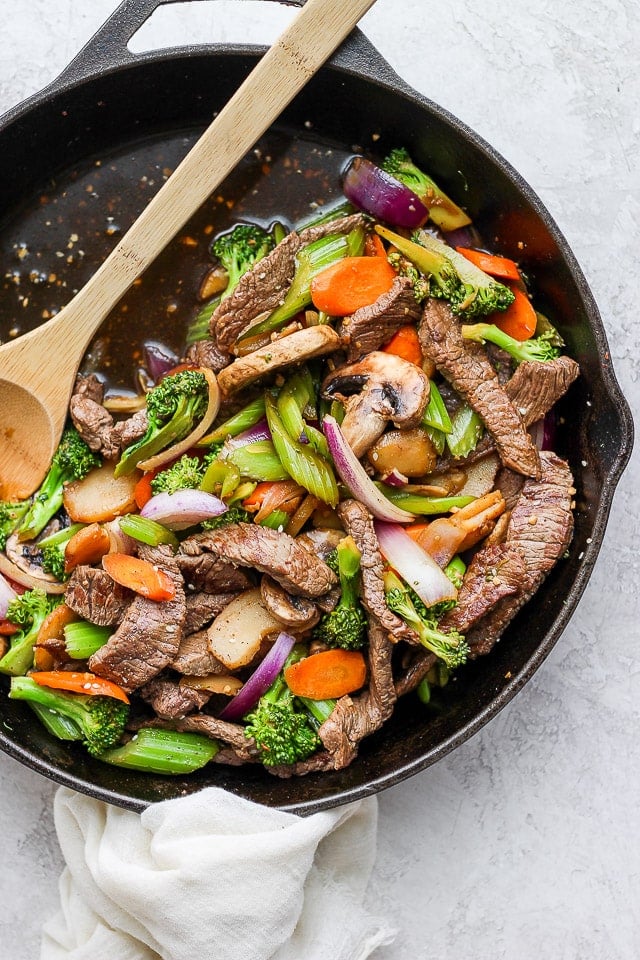 The finished steak stir fry in the skillet with a wooden spoon.