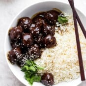 Cauliflower rice with teriyaki meatballs in a large white bowl with chopsticks.
