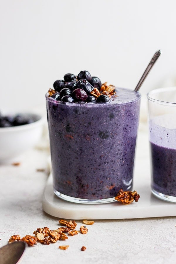 A blueberry banana smoothie in a glass topped with blueberries and granola. 