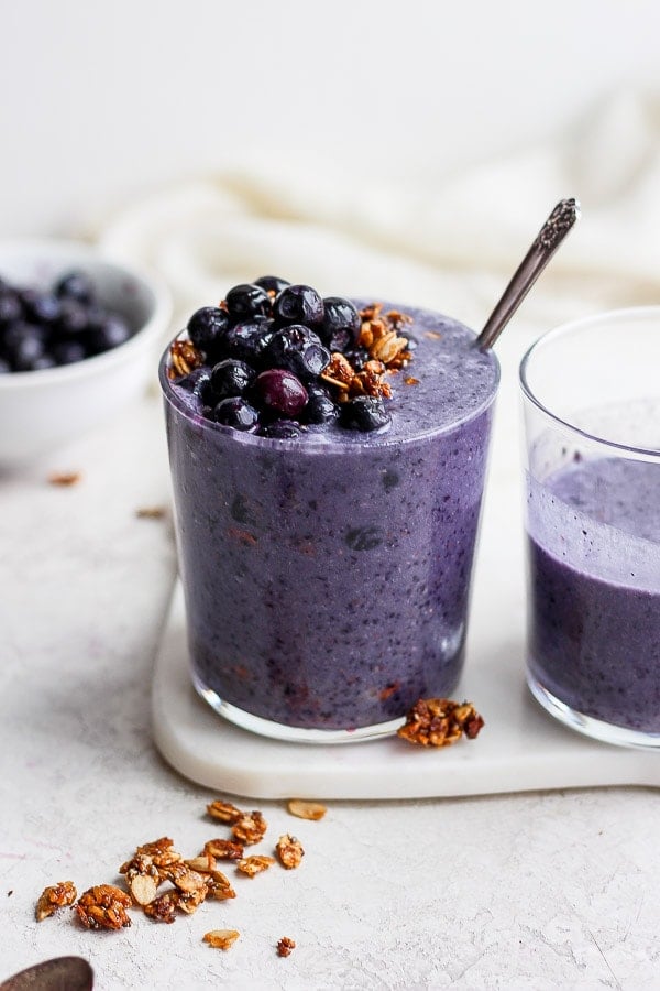 A blueberry banana smoothie in a glass topped with blueberries and granola. 