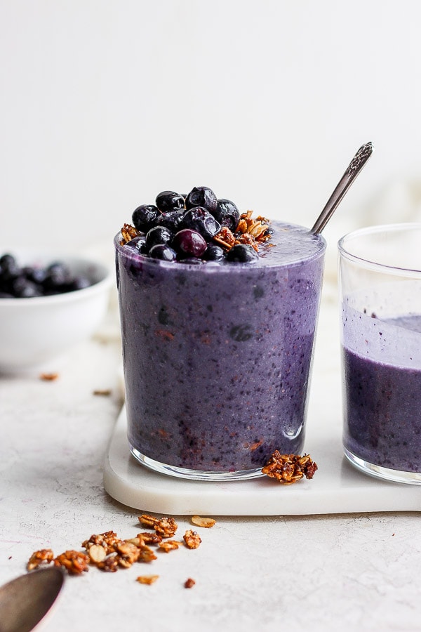 A blueberry banana smoothie in a glass topped with blueberries and granola. 