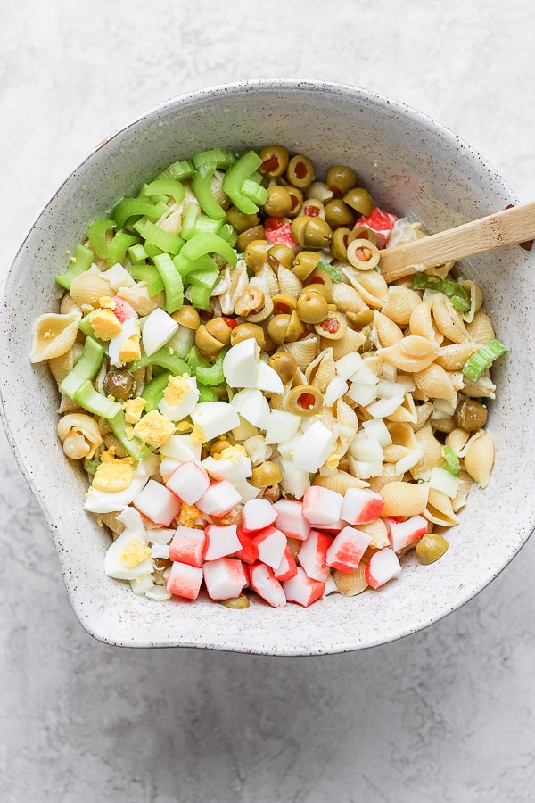 All the ingredients for an easy crab pasta salad in a bowl with a wooden spoon.