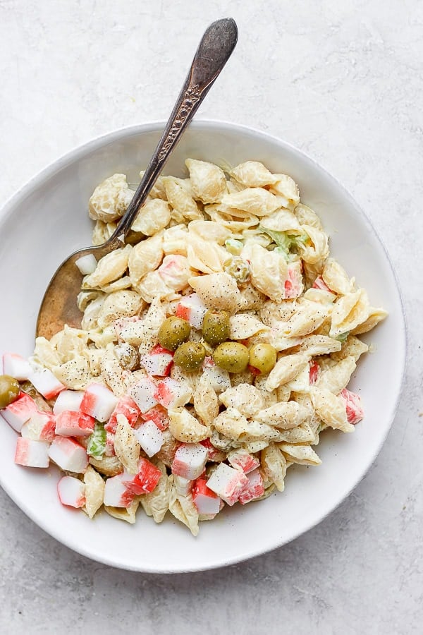 Crab pasta salad in a white bowl with a spoon.