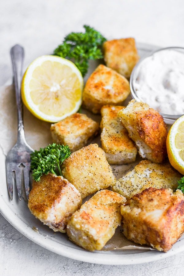 A plate of fish nuggets with some tartar sauce and a fork.