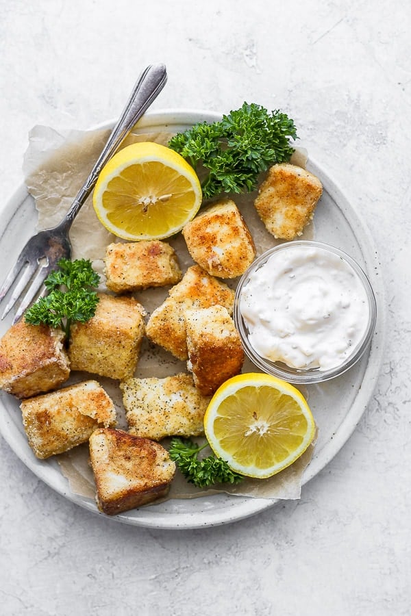 A white plate with some parchment paper and the fully baked fish nuggets.