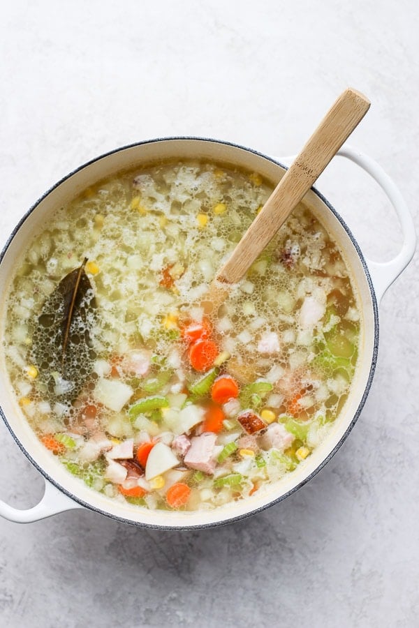 Ham bone soup in a dutch oven with a large wooden spoon.